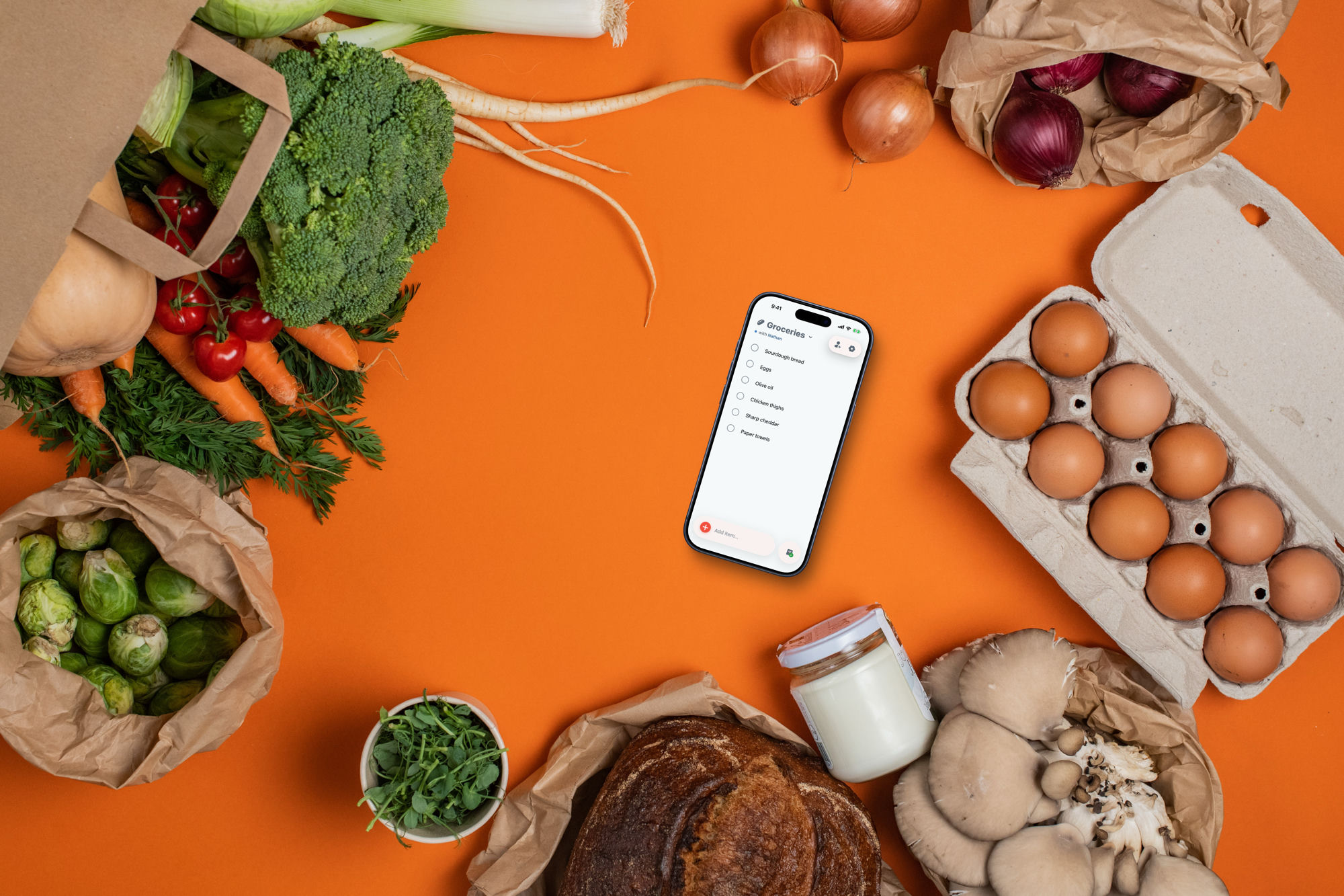 The Stores grocery list open on a phone, surrounded by fresh vegetables, eggs, bread and milk.